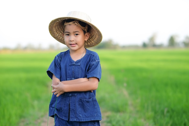 Un paysan vêtu d'une chemise traditionnelle et d'un chapeau de paille se tient les bras croisés et sourit sur le terrain.