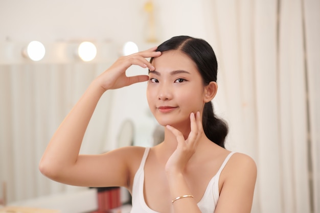 Peau parfaite. Cheerful Brunette Woman Touching Face à la recherche dans le miroir