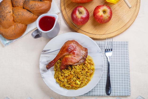 Épeautre avec une cuisse de canard dans une assiette sur la table de fête pour Roch Hachana à côté des friandises rituelles du vin et de la challah