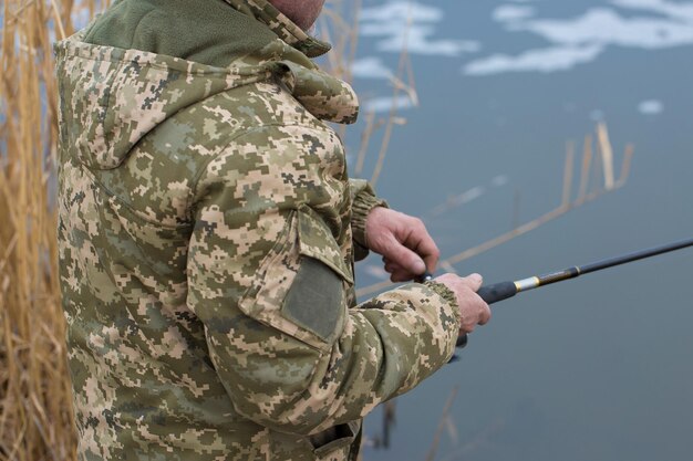 Pêche dans les roseaux pour filer sur une eau calme Un homme en tenue de camouflage par temps frais