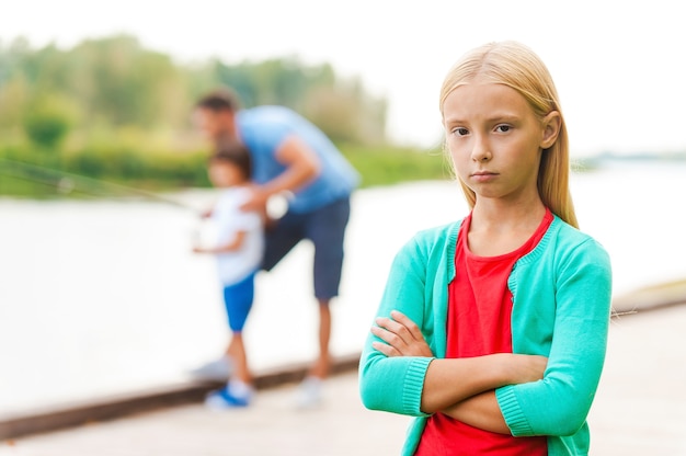 La pêche est trop ennuyeuse pour moi ! Petite fille déprimée gardant les bras croisés et regardant la caméra pendant qu'un homme avec un petit garçon pêchant en arrière-plan