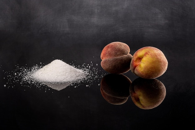 Pêches et un tas de sucre blanc ou de poudre blanche sur une surface noire