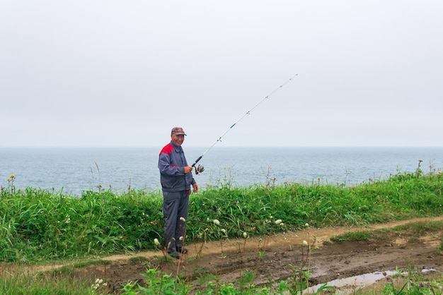 Un pêcheur âgé vérifie sa canne à pêche au bord de la mer