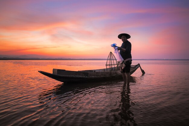 Pêcheur asiatique avec son bateau en bois dans la nature rivière tôt le matin avant le lever du soleil