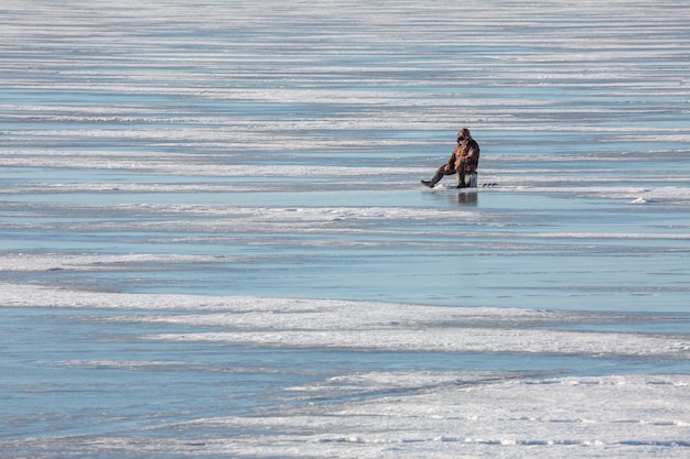 Pêcheur assis près du trou dans la glace du golfe de Finlande.