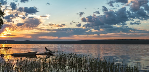 Un pêcheur attrape des poissons de la jetée au coucher du soleil Loisirs sur le lac Panorama