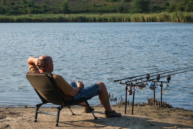 Pêcheur avec une boisson chaude dans une tasse attendant une bouchée avec du matériel de pêche à la carpe. Le pêcheur pêche