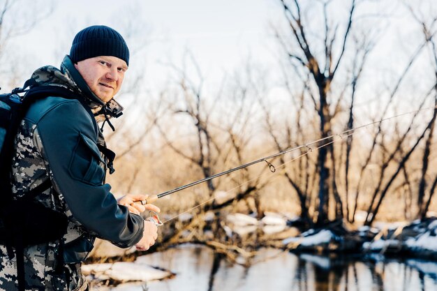 Un pêcheur avec une canne à pêche attrape du poisson sur la rive d'une rivière enneigée au début du printemps.