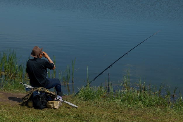 Pêcheur avec canne à pêche attraper du poisson, assis au bord de la rivière.