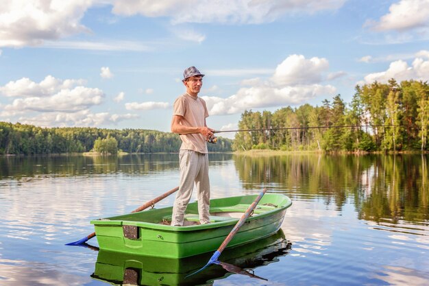 Le pêcheur avec des cannes à pêche pêche dans un bateau en bois sur fond de belle nature et de lac ou de rivière. Camping tourisme relax voyage concept d'aventure mode de vie actif