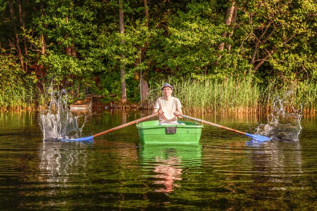 Le pêcheur avec des cannes à pêche pêche dans un bateau en bois sur fond de belle nature et de lac ou de rivière. Camping tourisme relax voyage concept d'aventure mode de vie actif