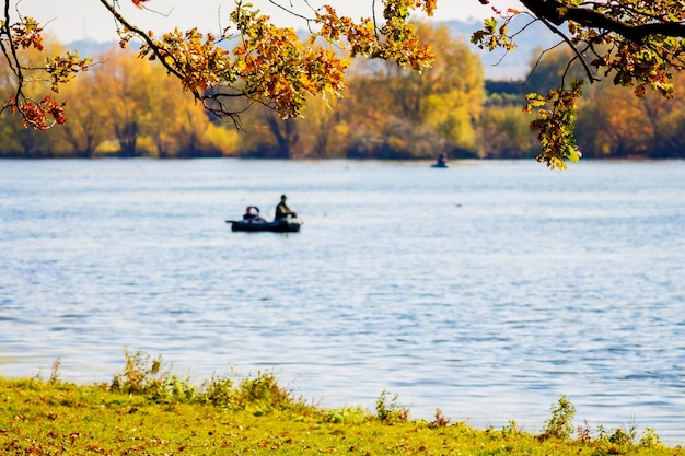 Pêcheur dans un bateau sur la rivière sur laquelle pendaient des branches avec des feuilles d'automne