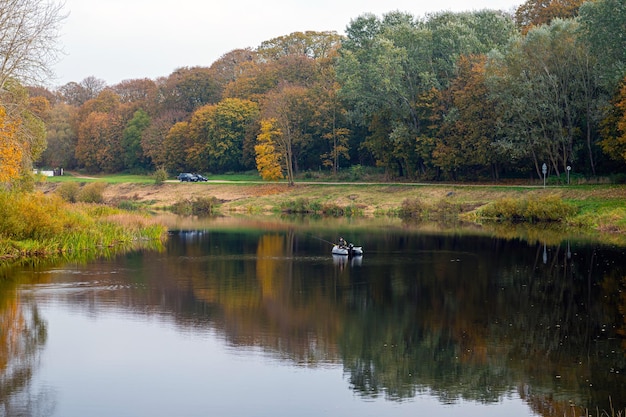 Pêcheur dans un canot pneumatique sur la rivière et arbres colorés sur le rivage par temps nuageux