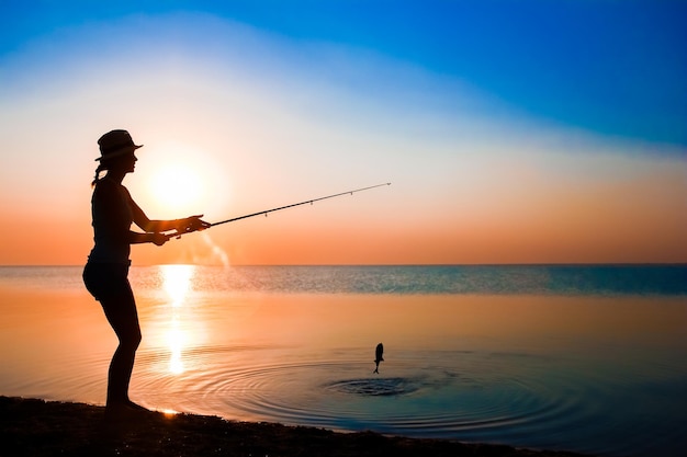 Un pêcheur fille heureuse attrape des poissons au bord de la mer sur la nature voyage silhouette