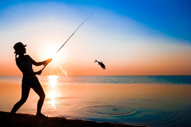 Un pêcheur fille heureuse attrape des poissons au bord de la mer sur la nature voyage silhouette