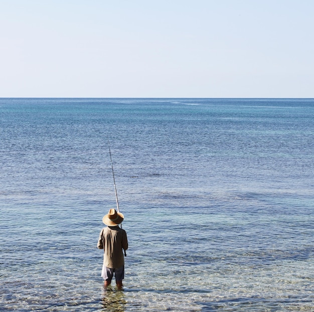 Pêcheur avec large chapeau de style oriental et canne à pêche vu de derrière Salento Pouilles Italie