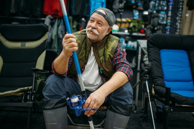 Le pêcheur masculin dans des bottes en caoutchouc tient la tige dans le magasin de pêche