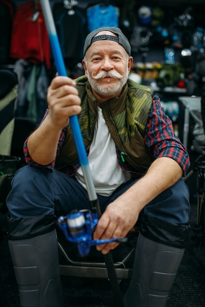 Le pêcheur masculin dans des bottes en caoutchouc tient la tige dans le magasin de pêche