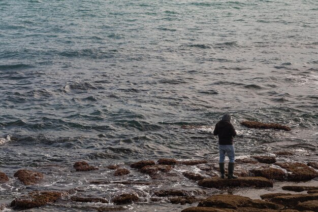 Un pêcheur masculin avec un imperméable noir attrape des poissons sur la mer pendant la saison d'hiver