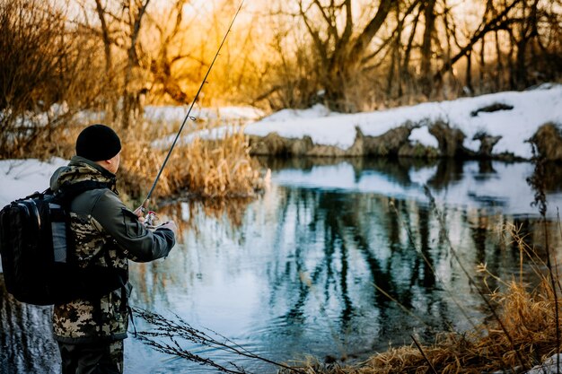 Un pêcheur pêchant avec une canne à lancer sur la berge en hiver