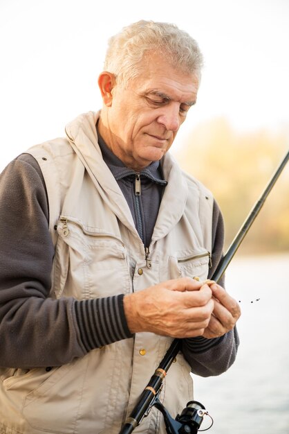 Un pêcheur senior accroche un ver sur un hameçon.