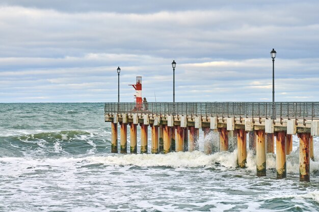 Pêcheur en tenue de camouflage et pêche sur la jetée avec phare. Paysage marin.