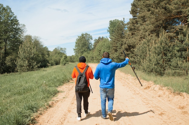 Pêcheurs allant pêcher sur la route, vue arrière. Deux personnes méconnaissables avec des cannes à pêche dans la nature