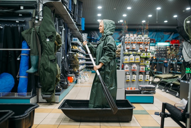 Pêcheuse dans un imperméable navigue sur un bateau dans un magasin de pêche, vue latérale, crochets et boules