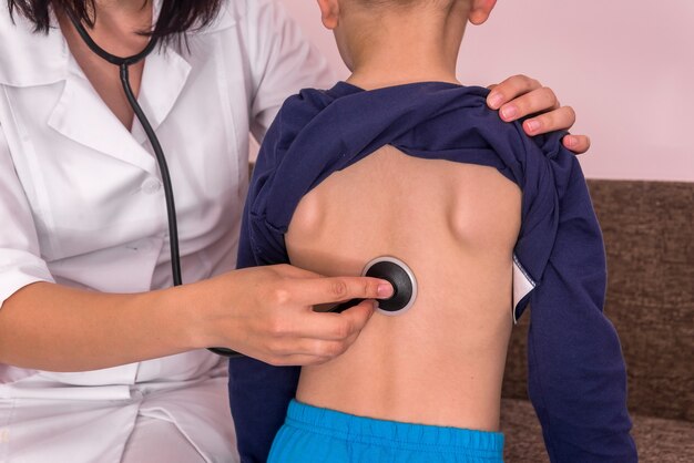 Pédiatre écoutant La Respiration Du Garçon Avec Un Stéthoscope Sur Le Dos