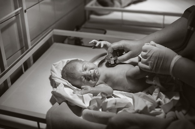 Un pédiatre examine un enfant à la clinique, une fille nouveau-née est allongée sur la table. Photo noir et blanc.