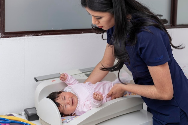 Pédiatre portant un bébé sur la balance dans son bureau pour peser