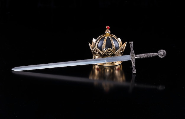 Épée médiévale et couronne sur fond noir isolé
