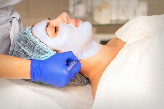 Peeling du visage chez l'esthéticienne. Traitement facial. L'esthéticienne applique un masque nettoyant sur la patiente.