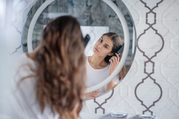 Peigner les cheveux. Une femme se peignant les cheveux près du miroir