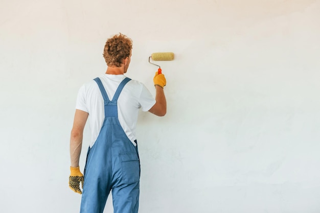 Peindre les murs Jeune homme travaillant en uniforme à la construction pendant la journée