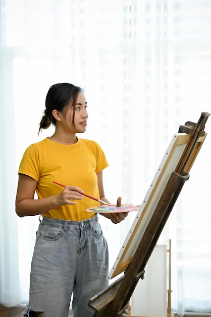 Peintre ou artiste asiatique talentueuse et professionnelle debout devant son chevalet en toile