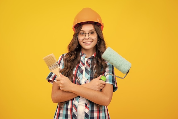 Peintre d'enfant adolescent dans le casque avec le pinceau de peinture Enfant dans le casque Peintre de constructeur d'enfant sur le chantier de construction Rénovation et réparation