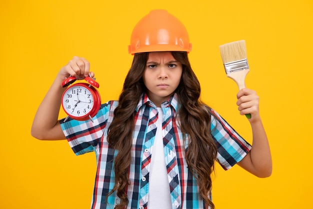 Peintre d'enfant adolescent sérieux en colère dans un casque avec un pinceau de peinture Enfant dans un casque et une alarme Peintre constructeur d'enfant sur le chantier de construction Temps de rénovation et de réparation