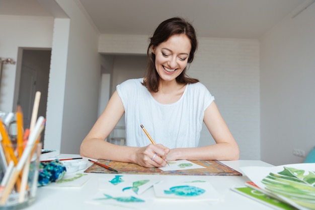 Peintre féminin attirant gai faisant des croquis à la table dans l'atelier