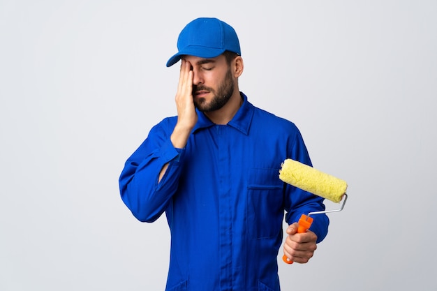 Peintre homme tenant un rouleau à peinture sur mur blanc avec maux de tête