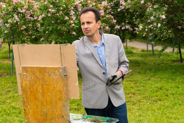 Peintre masculin mélancolique peinture un chef-d'œuvre sur un chevalet et chevalet peinture lors d'un cours d'art dans un parc