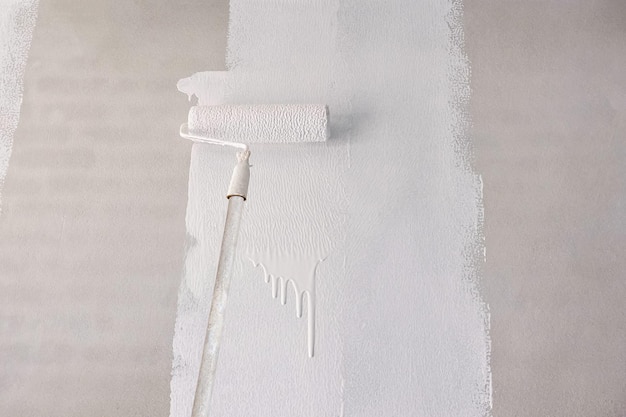 Photo peinture d'amorçage de couleur blanche sur un mur de béton avec une brosse à rouleaux à poignée longue sur un chantier de construction