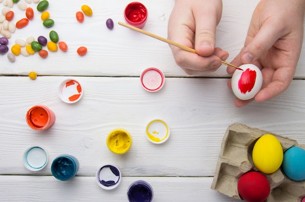 Peinture des oeufs de Pâques sur une table en bois avec de la peinture et des bonbons