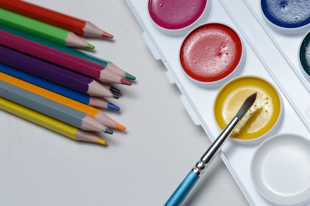 Peintures multicolores pour dessiner dans une palette, un pinceau et des crayons