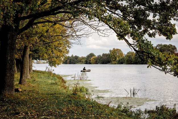 Peizaz avec rivière et forêt. Arbres au-dessus de l'eau. Pêcheur dans un bateau au milieu d'une rivière