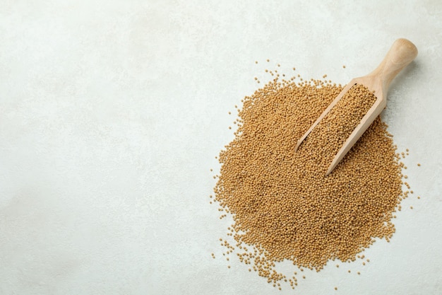 Pelle en bois avec des graines de moutarde sur fond texturé blanc