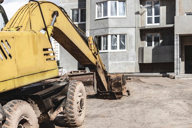 Une Pelle Sur Chenilles Lourde Avec Un Grand Godet Se Prépare à Travailler Devant Une Maison à Panneaux En Construction .. L'équipement De Construction Lourd Pour Les Travaux De Terrassement. Excavatrice De Carrière.