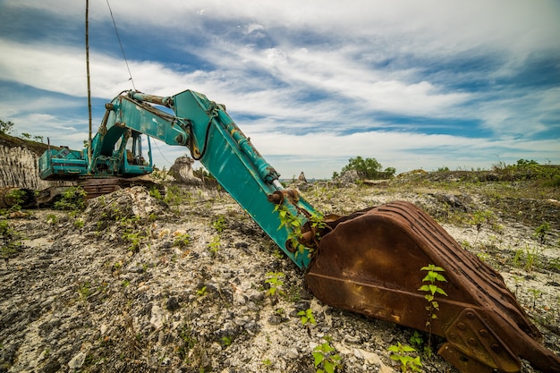 Pelle excavatrice lourde, ancienne et cassée avec pelle debout sur une colline avec des rochers