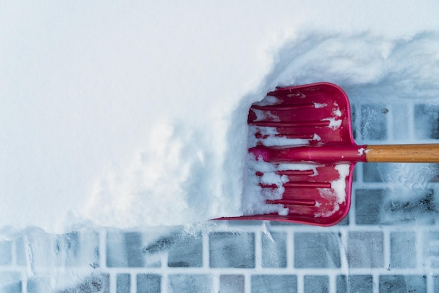 Photo une pelle à neige rouge à poignée de bois nettoie une épaisse couche de neige d'une dalle de pavage