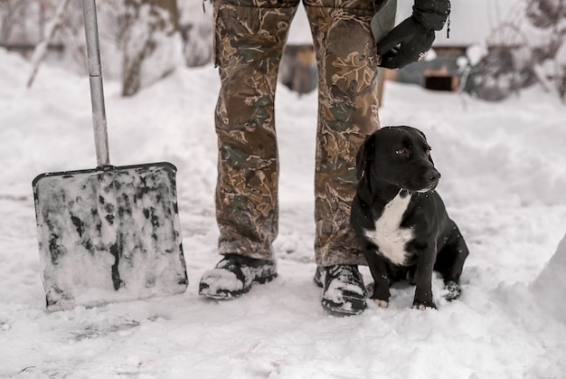 Une pelle pour déneiger se tient à côté des pieds d'un homme en bottes d'hiver